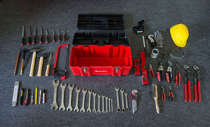 Monteurs-Werkzeuge liegen aufgereiht auf dem Boden vor einem roten Werkzeugkoffer