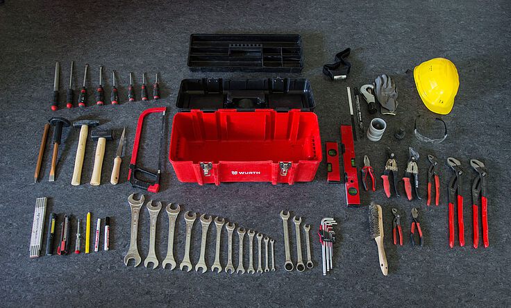 SHK-Kundendiensttechniker (m/w/d) Monteurs-Werkzeuge liegen aufgereiht auf dem Boden vor einem roten Werkzeugkoffer